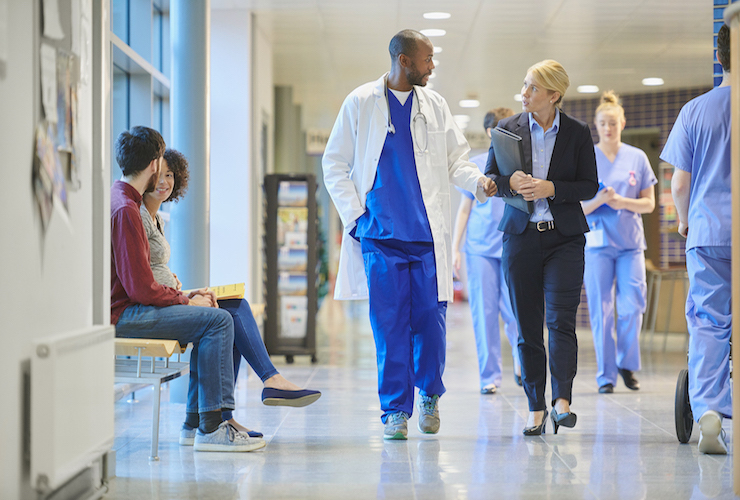 Image of people sitting and HCPs walking in the hallway of hospital.